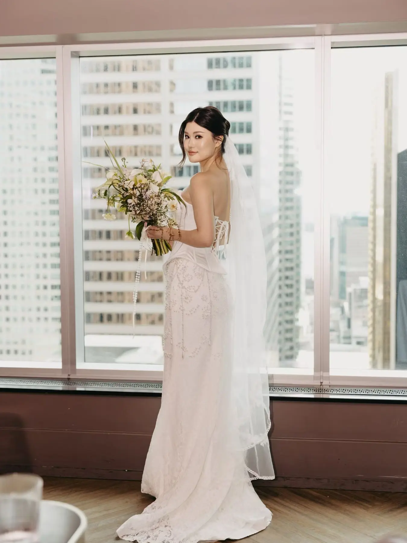 Full-length bride beside city windows by Angelina