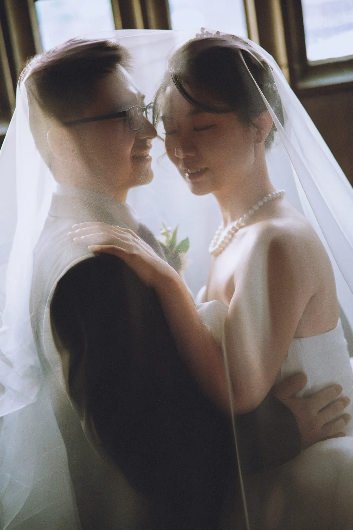 Veiled newlyweds in a quiet window portrait