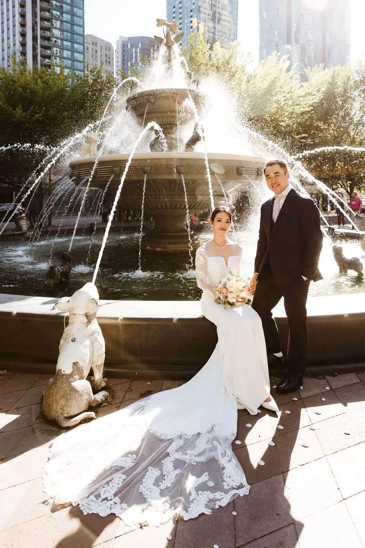 Newlyweds beside a sunlit city fountain