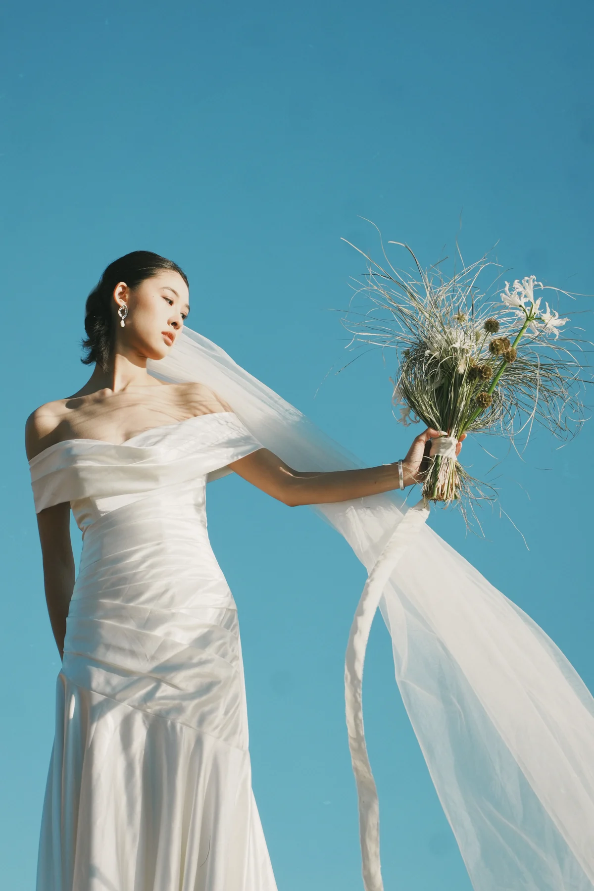 Bride holding a wildflower bouquet against a blue sky