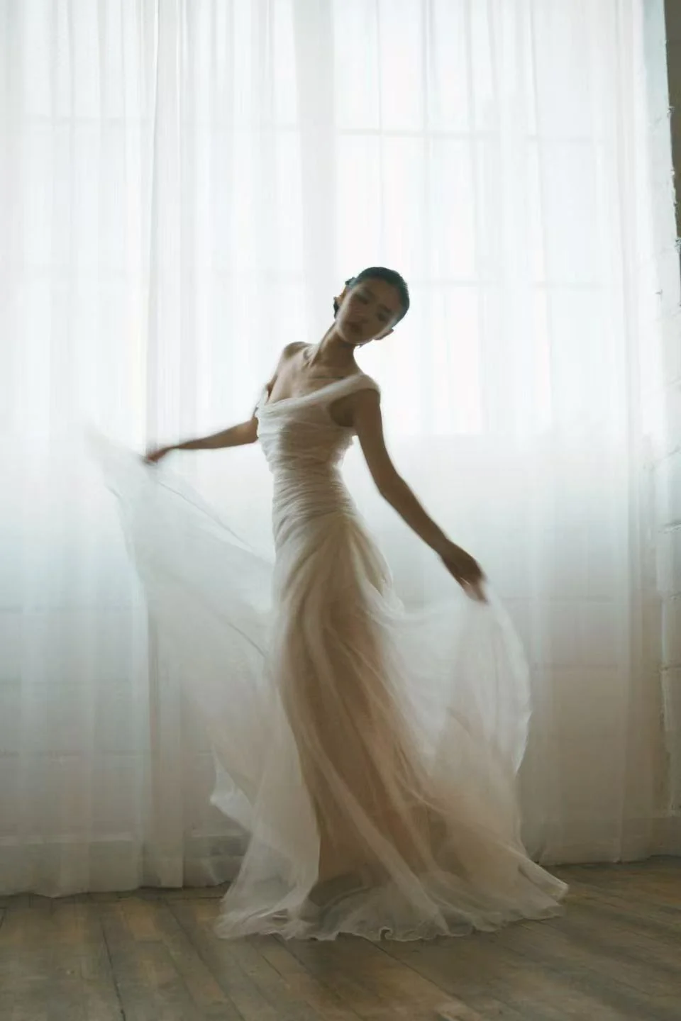 Bride in a flowing gown beside softly lit curtains